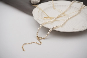 Detail of freshwater mini pearl necklace with golden lobster clasp on white relief plate