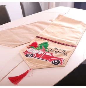 Detail of Christmas burlap table runner with red truck, gnome patterns and festive fringes