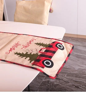 Close-up of Merry Christmas table runner with red truck and green tree pattern on linen