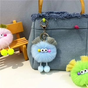 Close-up of blue monster plush keychain with googly eyes hanging on a denim bag strap