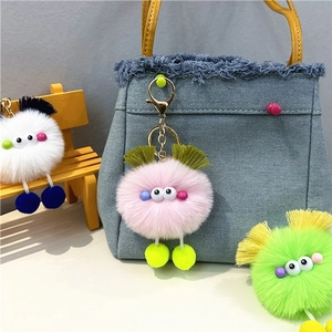 Detail of colorful plush monster keychains with tassels used as bag charms on a mini chair