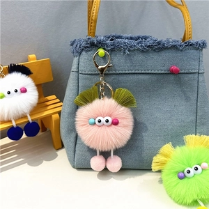 Cute plush monster bag charm with pom-pom legs on blue denim bag and mini wooden stool