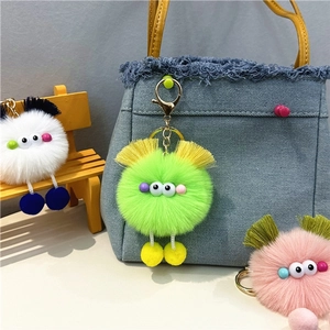 Close-up of cute plush monster charm with golden clasp on denim bag featuring tassels