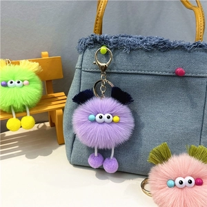 Detailed plush monster keychains in purple, green, and pink colors hanging on a denim bag