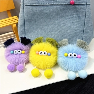 Three cute plush monster keychains with big eyes and colorful tassels on a denim bag
