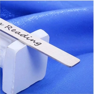 Macro shot of stainless steel bookmark with engraved reading script on blue fabric