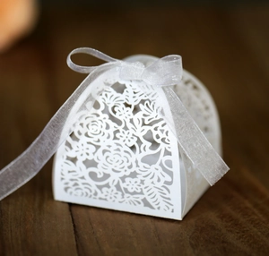 Close-up of white laser-cut wedding favor box with intricate floral hollow design and ribbon