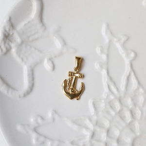 Macro shot of 18K gold-plated anchor pendant on decorative ceramic tray detail