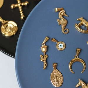 18K gold plated titanium steel rose, plane, and unicorn pendants on a blue tray
