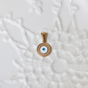 Macro view of a round 18K gold evil eye pendant with blue enamel and textured gold border
