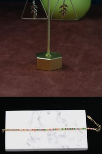 Detail of leaf earrings on gold stand and rainbow crystal bracelet on marble base