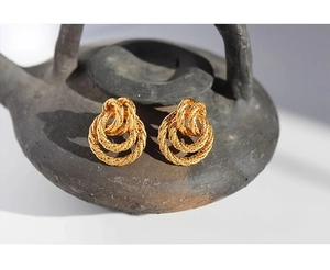 Macro shot of gold twist earrings with vintage texture on dark textured pottery