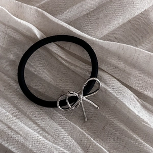 Detail of a black elastic hair tie with a vintage silver bow charm on beige fabric
