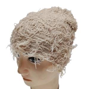 Detail showing the textured fringe material and knit fabric of the beige beanie cap
