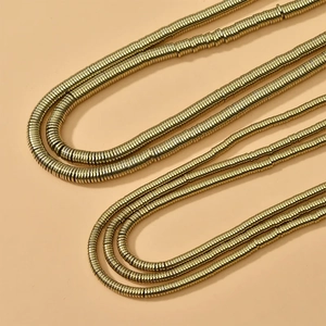 Golden multi-layer disc bead necklace with a sleek metallic finish on beige backdrop