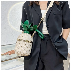 Detail of pineapple crossbody bag with gold studs and green leaf top on a black blazer