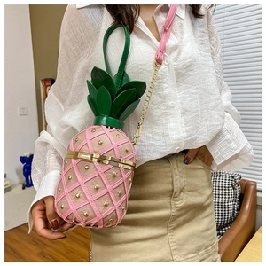 Detail of pink pineapple shoulder bag with gold rivets worn by a model in a cozy home setting
