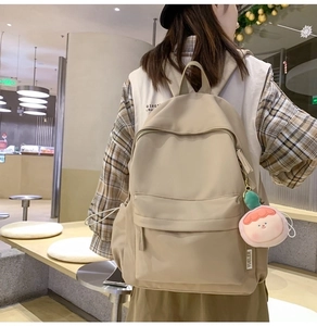 Rear view of model wearing beige minimalist backpack with pink charm in a mall