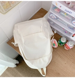 Detail view of a cream white nylon backpack with side drawstring pockets on a wooden desk