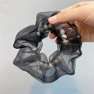 Detail eines schwarzen Organza-Haargummis mit weißen Perlen auf hellem Hintergrund