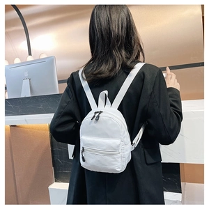 Rear view of a model wearing a white mini nylon backpack with dual zipper compartments