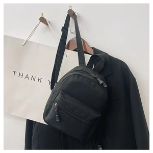 Hanging black nylon mini backpack featuring adjustable straps and front zip pocket detail