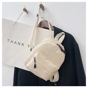 Classic beige nylon backpack for women hanging with a black blazer on a minimalist background
