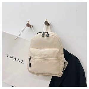 Detailed view of cream nylon mini backpack hanging on wooden hook with minimalist props