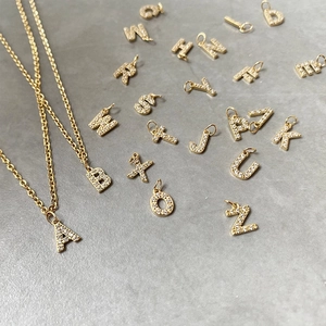 Golden stainless steel A-Z initial pendants with zircon crystals on a grey background