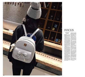 Macro shot of grey PU leather backpack featuring bow detail and white bear pendant