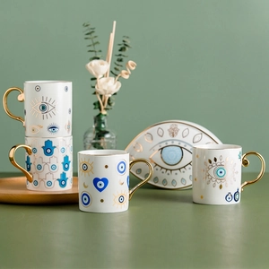 Close-up of ceramic mugs and plate with blue evil eye patterns and gold hamsa hand details