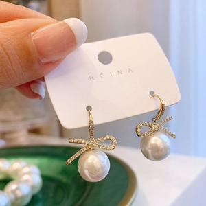 Detail of gold bow earrings with sparkling rhinestones and elegant white pearl drop