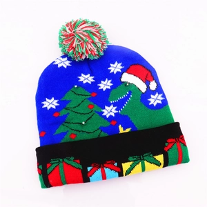 Close-up of blue knitted Christmas hat featuring cartoon dinosaurs and a white pom-pom