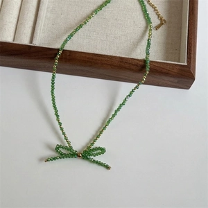 Macro shot of green faceted crystal beads necklace with a delicate bow pendant and gold beads