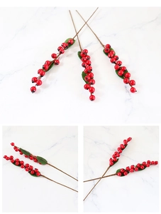 Close-up detail of artificial red berries with green leaves on white marble background