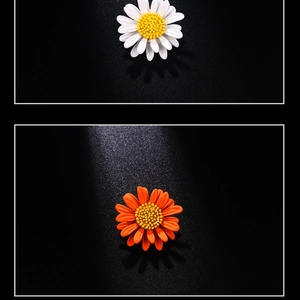Detail of white and orange enamel daisy brooches on a contrast black background