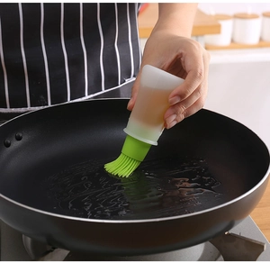 Silicone oil brush bottle with scale being used to apply oil on a black frying pan