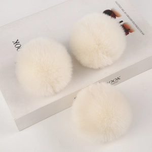 Detailed view of three soft ivory faux rabbit fur pompoms on a minimalist book background