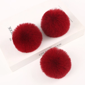 Close-up of three burgundy faux rabbit fur pom poms on a white decorative book