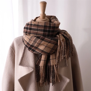 Detail of brown and black plaid scarf with fringe on a beige coat mannequin