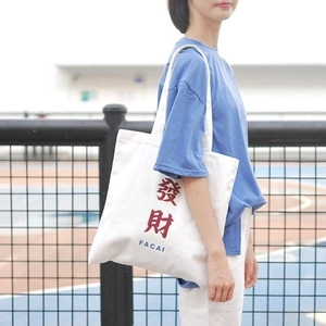 Detail view of white canvas tote bag with red FACAI print shown on outdoor shoulder strap