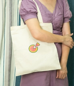 Close-up of a cream canvas tote bag featuring a small embroidered watermelon on a model