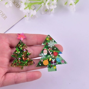 Handheld view of green acrylic Christmas tree earrings with glitter and festive prints