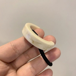 Detail of a high-elastic black hair tie featuring a beige marble-pattern resin C-ring