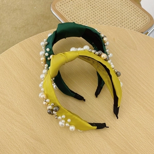 Close-up of dark green and mustard yellow knot headbands with faux pearls on fabric