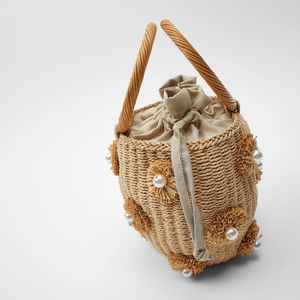 Detailed view of straw bucket bag with floral accents and faux pearl decorations