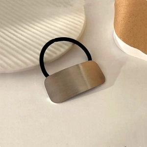 Detail of silver metal rectangle charm on black elastic hair tie with a minimalist design