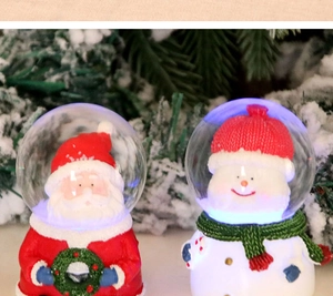Close-up of glowing Santa and Snowman resin glass snow globes for Christmas decor