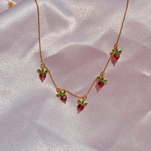 Macro shot of gold necklace featuring five strawberry pendants with red and green zircons