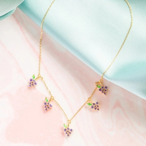 Gold chain necklace with purple grape pendants and green leaf zircons on pink background